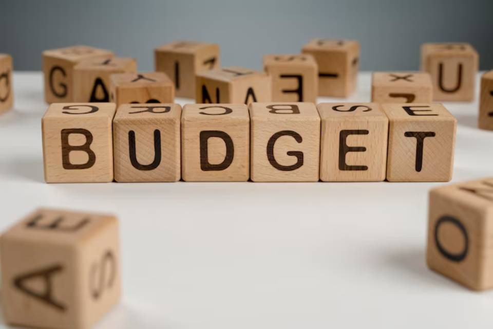 Wooden letter blocks spelling BUDGET surrounded by scattered letters on a white surface, emphasizing financial planning.