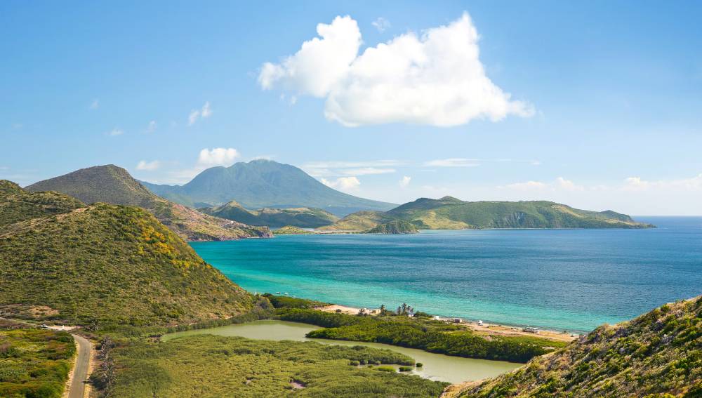 Breathtaking coastal landscape featuring lush hills, a serene blue sea, and a distant volcanic mountain under a clear sky.