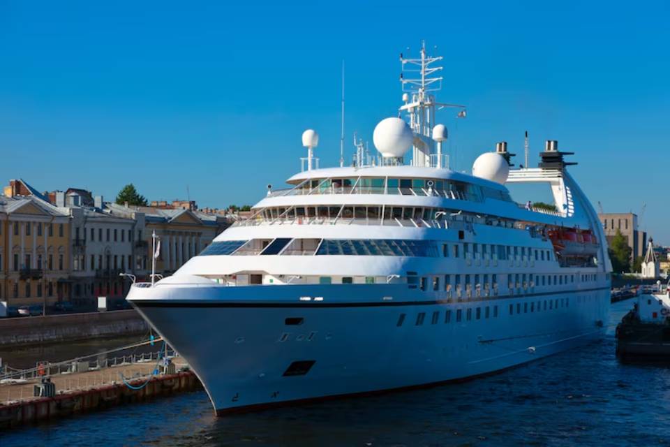 A luxury cruise ship docked alongside historic buildings, set against a clear blue sky and reflecting on the calm water.