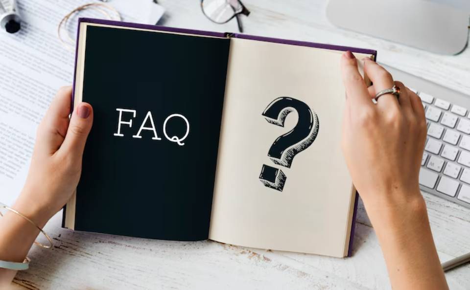 A person holding an open book displaying FAQ on one page and a large question mark on the opposite page, set on a desk.