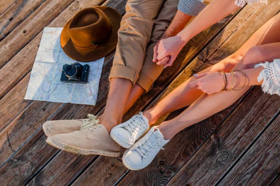 A couple holding hands on a wooden deck, with a vintage camera and map nearby, showcasing their relaxed, adventurous vibe.