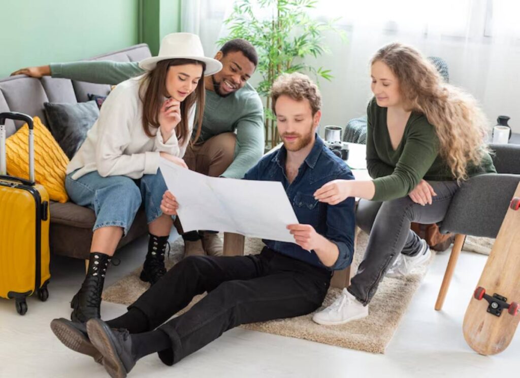 A group of friends gathers in a stylish living room, examining a map on the floor while sitting around a cozy sofa.