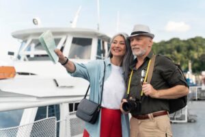 A couple stands together on a boat, smiling and taking a selfie while holding a map. The background features water and trees.