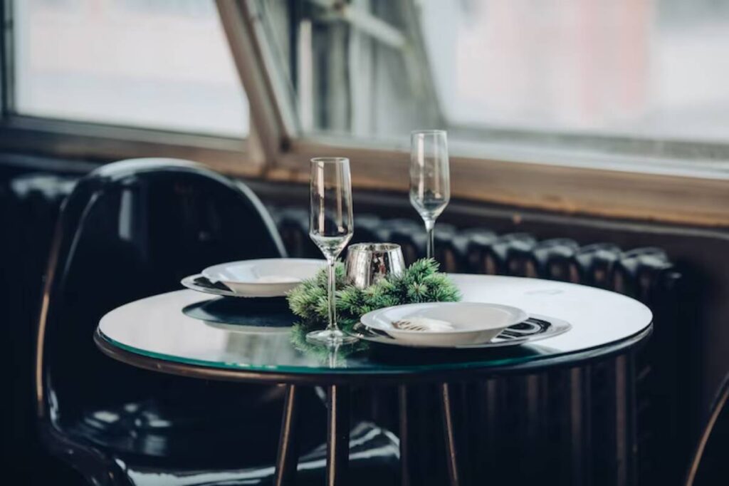 A cozy dining table set with white plates, elegant flutes, and green decor, illuminated by natural light, creating a festive ambiance.