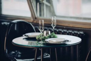 A cozy dining table set with white plates, elegant flutes, and green decor, illuminated by natural light, creating a festive ambiance.