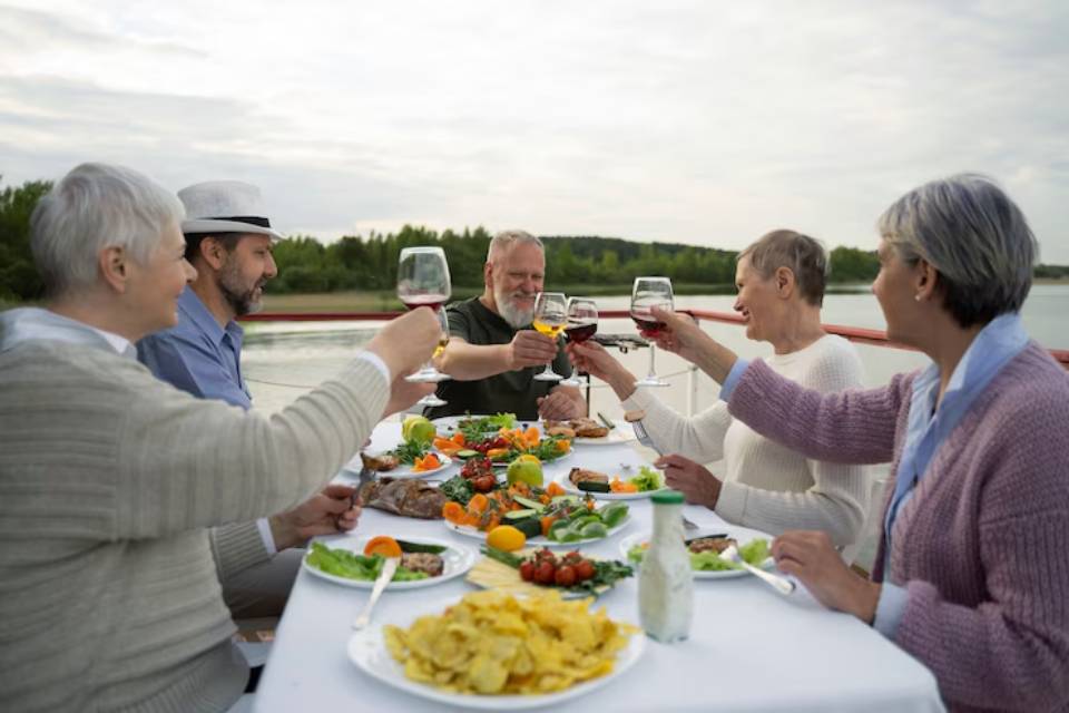 A group of friends celebrates over a festive outdoor meal on a boat, raising glasses filled with wine amidst a scenic backdrop.