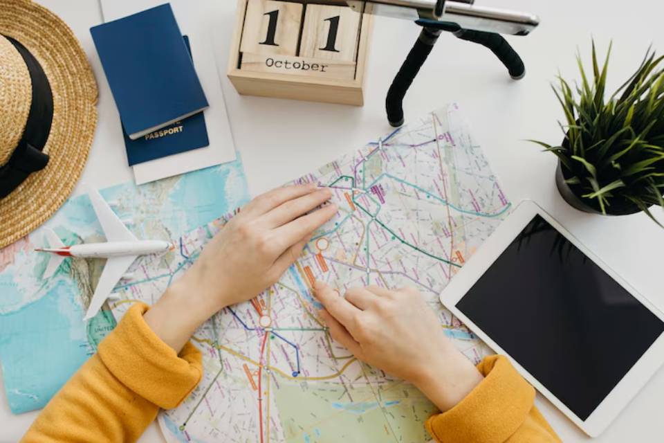 A traveler studies a colorful map, surrounded by a passport, hat, airplane model, tablet, and a calendar showing October 11.