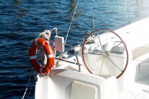 Top view of a yacht's steering wheel with a life ring nearby, set against a backdrop of deep blue water.