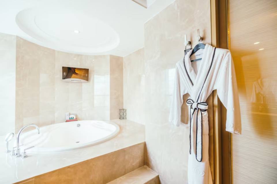 Luxurious bathroom featuring a round bathtub, wall-mounted TV, and a plush white robe hanging on the door. Elegant marble finishes throughout.