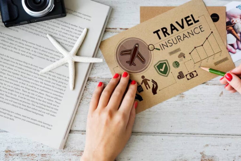 A hand with red nails holds a green pencil on a travel insurance brochure beside a camera, starfish, and a book.