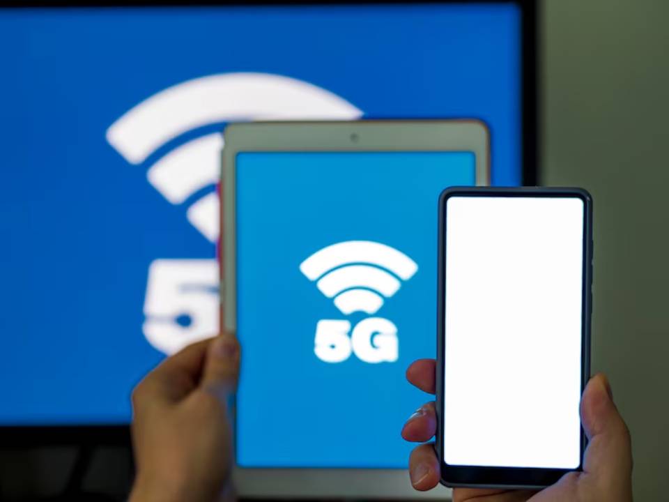 A person holds a smartphone and a tablet, both displaying a prominent 5G logo against a blue background.
