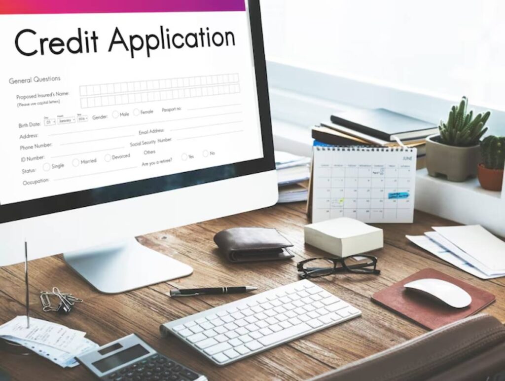 A computer screen displays a credit application form, surrounded by office supplies and a calendar on a wooden desk.